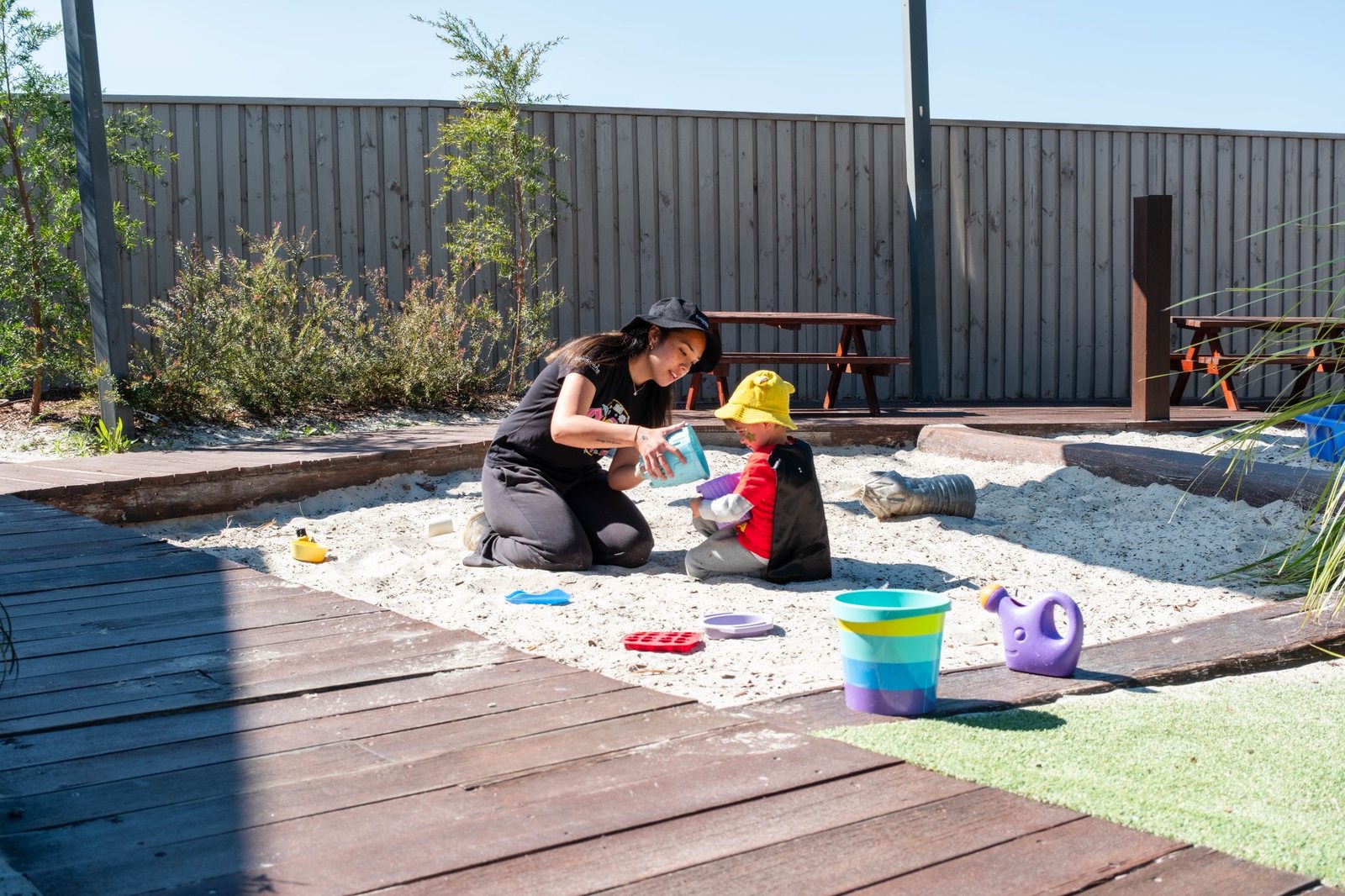 An educator and children playing beside the sandpit at Expeditions Underwood